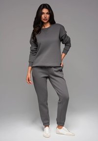 Grauer Hoodie und passende Jogginghose, aus weichem Stoff gefertigt, mit gerippten Bündchen und lässigem Schnitt. Weiße Sneaker runden das Outfit ab.