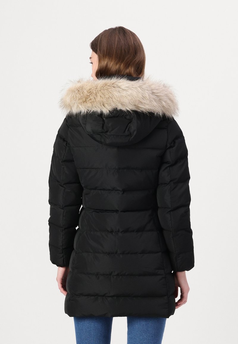Zwarte pufferjas met een nepbont capuchon, gewatteerd design en lange mouwen. De jas heeft een gladde textuur en reikt tot halverwege het bovenbeen, geschikt voor koud weer.