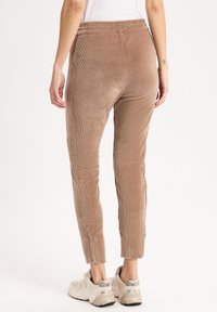 Lichte bruine corduroypants met verticale ribbels, elastische tailleband, slim fit, gestikte details, gecombineerd met beige sportschoenen.