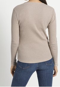 Beige långärmad ribbad topp med rund halsringning, åtsittande passform och textilstruktur. Buren med mörkblå jeans, sedd bakifrån.