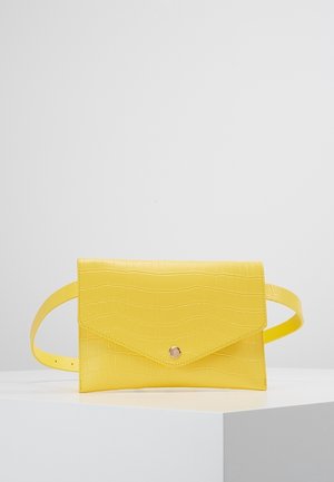 Bolso tipo cinturón de cuero falso de cocodrilo amarillo con solapa de sobre y cierre de botón a presión reposando sobre una superficie blanca.