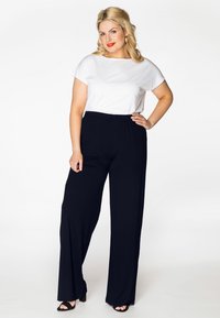 Witte top met korte mouwen, gecombineerd met zwarte wijde broek. De outfit heeft een luchtige pasvorm en een zachte stof. Zwarte hoge hakken maken de look compleet.