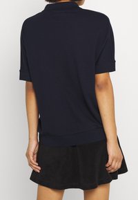 Mörkblå polo med korta ärmar, huvudsakligen tillverkad av bomull, med en ribbad krage och en avslappnad passform.