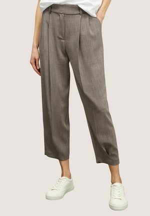 Vrouw draagt grijze, hooggetailleerde, losvallende cropped broek met plooien aan de voorkant, gecombineerd met witte sneakers en een wit ingestopt topje.