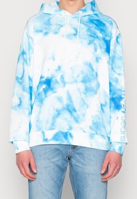 Felpa con cappuccio in bianco e blu con motivo tie-dye, realizzata in tessuto morbido. Presenta una tasca a marsupio e un logo stampato sulla manica.