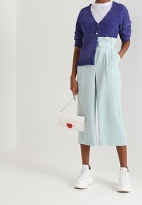 Fialový pletený kardigan, bílý tričko, světle modré široké kalhoty, bílá taška s červeným srdcem a masivní bílé tenisky.