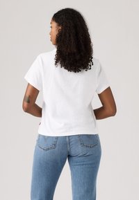 T-shirt en coton blanc à manches courtes, vue de dos, associé à un jean denim bleu clair avec poches arrière et un léger effet délavé.