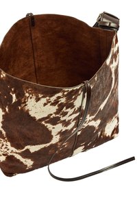 Torba z brązowej i kremowej skóry bydlęcej o miękkiej teksturze, otwartym wnętrzu oraz ciemnym skórzanym pasku. Na zewnętrznej stronie znajdują się organiczne wzory.