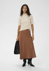 Beige ribstrikket kortærmet rullekrave kombineret med en brun nederdel med hvide polkaprikker, suppleret med sorte knælange støvler og en sort taske.