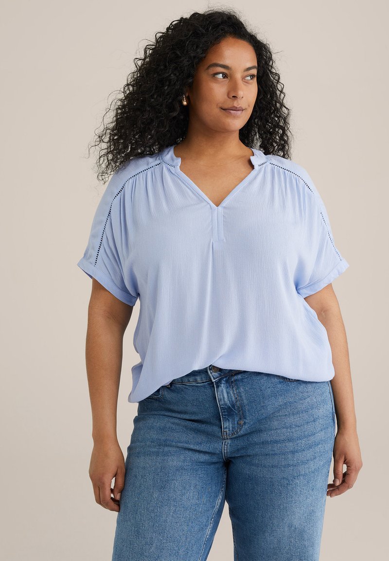 Top azul claro de manga corta con escote en V, hombros fruncidos y pequeños detalles de ojales en las mangas. Tela suave y texturizada.