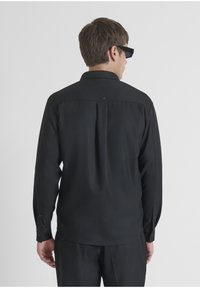 Zwarte longsleeve shirt, glad materiaal, knoopmanchetten, subtiele achterlabel, standaard kraag, normale pasvorm, geen patronen of graphics.