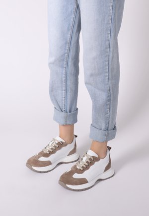 Białe i taupe zamszowe sneakersy z teksturowaną siateczkową górą, okrągłym czubkiem i beżowymi sznurówkami. Noszone z podwiniętymi jasnoniebieskimi dżinsami.