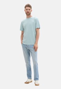 Hellblaues Baumwoll-T-Shirt mit kurzen Ärmeln und Rundhalsausschnitt, kombiniert mit hellblauen Jeans und beigen Sneakers.