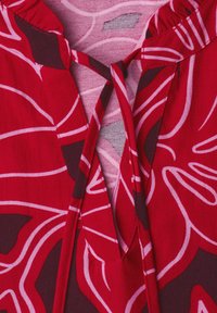 Tissu rouge avec motif floral abstrait rose foncé et clair et détail d'encolure nouée sur un vêtement.