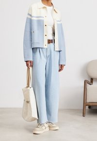 Jasnoniebieska krótka kurtka z kremowymi paskami, biała koszulka, luźne jasnoniebieskie dżinsy, beżowe trampki i beżowa torba typu tote.