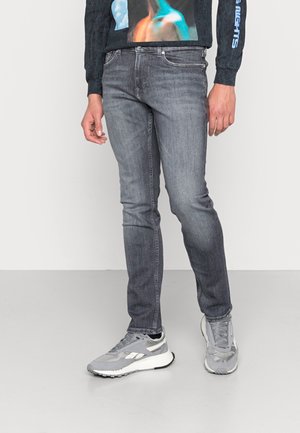 Jeans de mezclilla gris con un diseño ajustado, que presentan sutiles desgastes, cinco bolsillos y una cintura de altura media, combinados con zapatillas grises.
