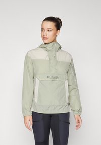 Letvægts hættepulloverjakke i lysegrøn og beige, med en frontlomme, justerbar snorhætte og elastiske manchetter.