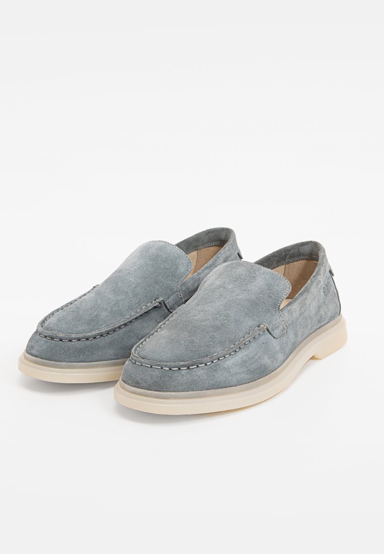 Bottines en daim gris à enfiler, avec un bout rond, une semelle en caoutchouc beige contrastante, et un minimum de couture le long des bords.