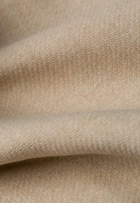 Beige wollen stof met een visgraatpatroon, met een zachte textuur en een lichte glans, gevouwen met zachte krommingen.