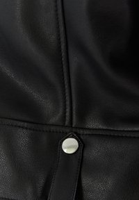 Musta nahkakangas, jossa on teksturoitu pinta. Varustettu metallisilla nepparilukoilla ja ommelluilla saumoilla reunoilla. Lähikuva.