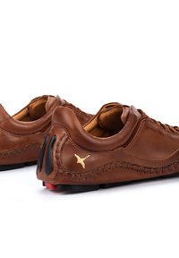 Braune Lederschuhe mit gesteppten Details, glatter Textur und einem kleinen goldenen Logo an der Seite. Schwarze und rote Akzente an der Sohle.