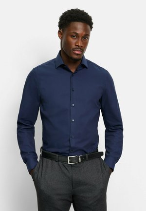 Navy blue dress shirt with long sleeves, button-up design, spread collar, textured fabric, paired with dark grey trousers and a black belt.