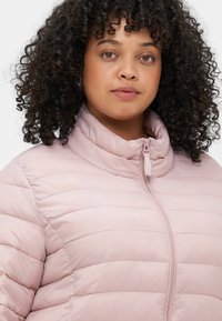Svetloružová zateplená bunda s horizontálnym prešívaním, vysokým golierom a predným zipsom. Hladká, lesklá tkanina s mäkkou textúrou.