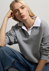Grijze sweatshirt met een witte kraag, zachte textuur, relaxte pasvorm en verlaagde schouders, gecombineerd met blauwe denim jeans.