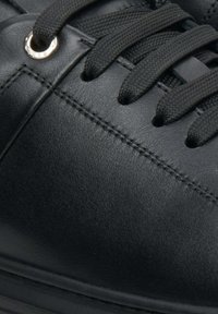 Czarne skórzane sneakersy z płaskimi czarnymi sznurowadłami, okrągłym metalowym oczkiem, subtelnymi przeszyciami i gładkim wykończeniem. Widoczny szczegół teksturowanej powierzchni.