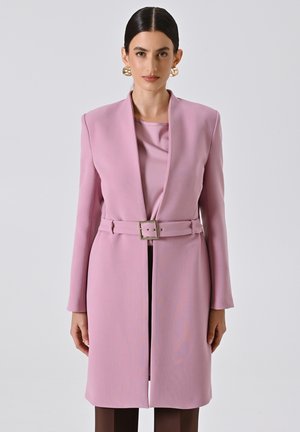 Cappotto a maniche lunghe di colore rosa tenue con vita regolabile e colletto a rever. Tessuto liscio, taglio dritto, termina appena sopra le ginocchia.
