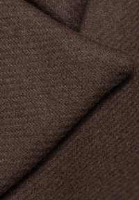 Brązowa tkanina wełniana o miękkiej, teksturowanej powierzchni z delikatnym wzorem. Materiał jest gęsto tkany, wydaje się ciepły i trwały.