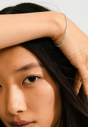 Silver bracelet with a textured finish, resting on a hand. Close-up of a face with long dark hair and a natural complexion.
