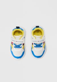 Modré a biele tenisky so žltými akcentmi, sieťovinovou textúrou, suchým zipsom a detailom šnúrky. Na vnútornej strane sú označené logom a číslom.