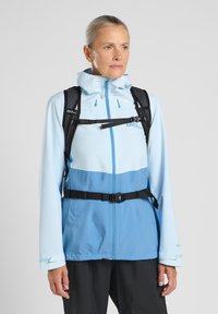 Veste imperméable bleu clair avec un panneau bleu plus foncé, des sangles noires ajustables et une capuche. Comprend une fermeture éclair à l'avant et un détail de logo.