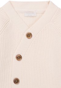 Kremowy sweter z dzianiny z dekoltem w kształcie V, z trzema drewnianymi guzikami i prążkowaną fakturą. Metka z napisem "noppies" z rozmiarem 56/1-2M.