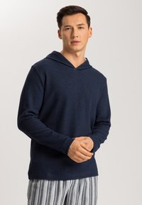 Sudadera con capucha de color azul marino y mangas largas, hecha de una tela suave, combinada con pantalones de pijama a rayas con líneas verticales en blanco y gris.