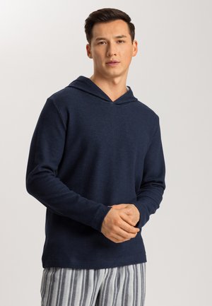 Sudadera con capucha de color azul marino y mangas largas, hecha de una tela suave, combinada con pantalones de pijama a rayas con líneas verticales en blanco y gris.