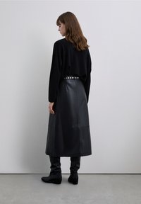 Fustă midi din piele neagră cu textură netedă, combinată cu un pulover negru larg. Ținuta include o curea cu ținte.