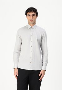 Light grey, long-sleeve shirt with a button-down collar, featuring a subtle checkered pattern and brown buttons, paired with dark pants.