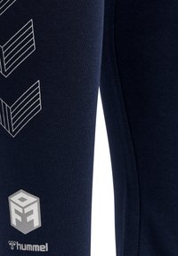 Marinblåa sweatpants i stretchigt tyg med ribbad textur. Har vitt geometriskt logo och detaljer på sidan.