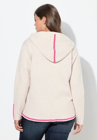 Hoodie beige clair avec un accent rose sur la couture arrière et les poignets. Il dispose d'une capuche avec cordon de serrage et d'une coupe décontractée, fabriqué à partir d'un matériau doux.