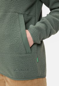 Pullover in pile verde con tessuto testurizzato, dotato di tasca frontale e logo ricamato sull'orlo. Polsini e orlo morbidi per il massimo comfort.
