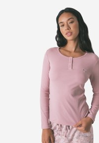 Maglietta a maniche lunghe rosa chiaro in tessuto a costine con scollatura rotonda, caratterizzata da dettagli con bottoni e un piccolo ricamo floreale.