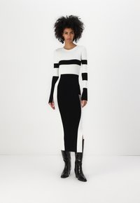 Stickad klänning med djärva svart-vita ränder, långa ärmar, en figurnära silhuett och slitsar på sidorna, kombinerad med glänsande svarta stövlar.