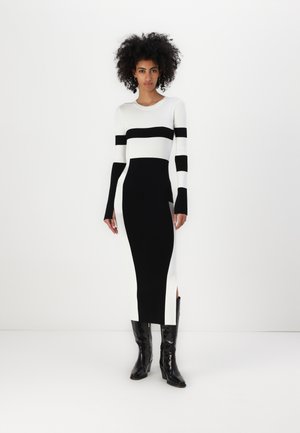 Abito in maglia con bold righe bianche e nere, maniche lunghe, silhouette aderente e spacco laterale, abbinato a stivali neri lucidi.