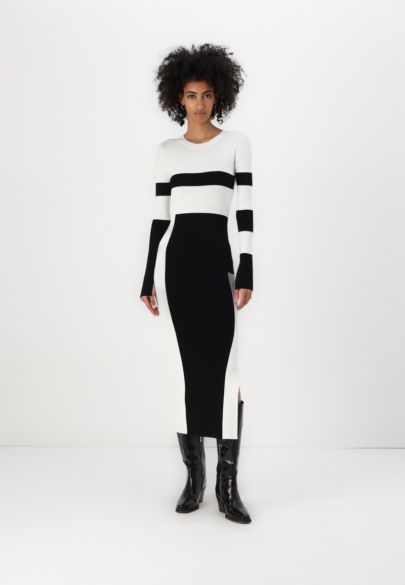 Stickad klänning med djärva svart-vita ränder, långa ärmar, en figurnära silhuett och slitsar på sidorna, kombinerad med glänsande svarta stövlar.