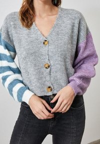 Grauer, gestrickter Cardigan mit gerippter Struktur, mit mehrfarbigen gestreiften Ärmeln in Blau, Weiß und Lila sowie Holzknöpfen.
