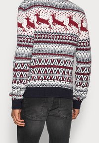 Stickad tröja med vit botten, röda renar, geometriska mönster samt marinblå ribbade muddar och fåll.