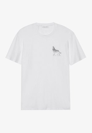T-shirt en coton blanc à manches courtes, présentant un graphique de loup noir et le texte "WALK ALONE" sous le design sur le côté gauche de la poitrine.