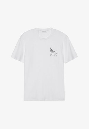 T-shirt en coton blanc à manches courtes, présentant un graphique de loup noir et le texte "WALK ALONE" sous le design sur le côté gauche de la poitrine.